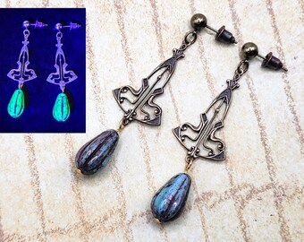 May include: A pair of dangle earrings with a blue and brown teardrop-shaped bead and a filigree design. The earrings are made of metal and have a bronze finish.