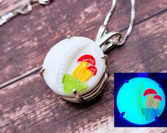 May include: A silver necklace with a white glass pendant featuring a yellow and red mushroom design. The pendant glows under a black light.