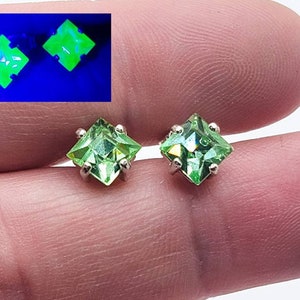 May include: A pair of silver stud earrings with square green gemstones. The gemstones glow under a black light.