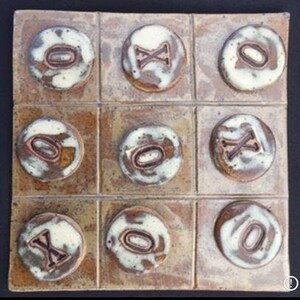 May include: A ceramic tile game board with nine squares. Each square has a circle with either an 'X' or an 'O' inside. The circles are white with brown outlines. The background of the board is brown with a mottled texture.