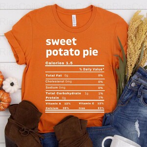 May include: Orange t-shirt with a white graphic of a nutrition label for "sweet potato pie". The label lists the calories as 1.5 and the percentage daily value for total fat, cholesterol, sodium, total carbohydrate, protein, vitamin A, vitamin C, calcium, and iron.