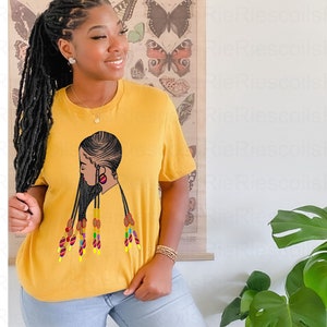 May include: A yellow t-shirt with a black and white illustration of a woman with long braids and colorful beads. The woman is wearing a red earring.