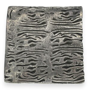 May include: A square metal tile featuring a dark gray, oxidized finish with a deeply textured, organic pattern of horizontal, wavy, and interconnected ridges that create a relief effect across the entire surface of the object.