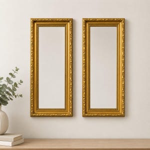 May include: Two rectangular wall mirrors featuring ornate gold frames with intricate beaded and scrollwork detailing. The mirrors have a vertical orientation and reflective glass surfaces, providing a clear view of the surrounding space.
