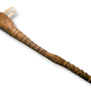 May include: A brown wooden club featuring a long, textured handle wrapped with leather strips. The head of the club is rounded and includes two sharp, light-colored, pointed protrusions extending from the top, resembling animal teeth or claws.