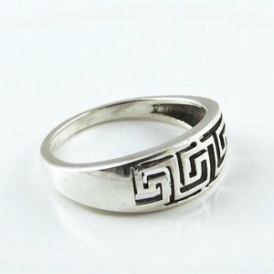 May include: A silver ring with a Greek key design. The ring is wide and has a smooth, polished finish.