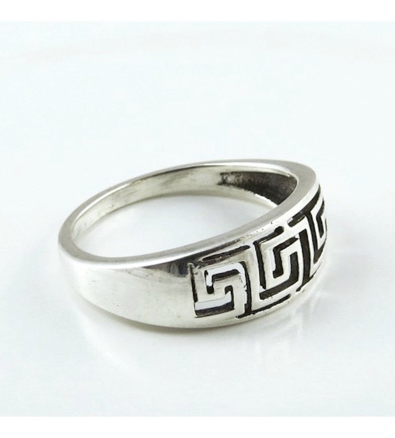 May include: A silver ring with a Greek key design. The ring is wide and has a smooth, polished finish.