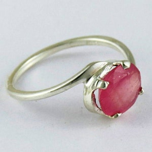 May include: A silver ring with a pink oval gemstone set in a prong setting.