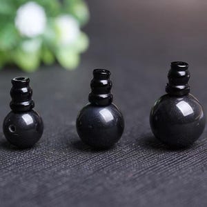 Peut inclure: Trois perles noires et brillantes de forme sphérique, surmontées d'un cylindre. Les perles varient en taille, la plus petite à gauche et la plus grande à droite. Sur un fond sombre et texturé.