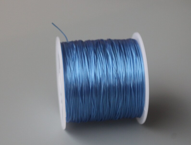 Peut inclure: Une bobine de cordon &eacute;lastique bleu clair, enroul&eacute;e autour d'une bobine en plastique blanc.