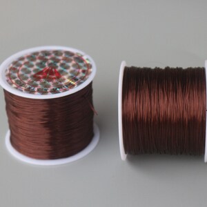 May include: Two spools of brown elastic cord, wound on white plastic spools. The spools have a holographic label with the text "Elastic Cord & String".