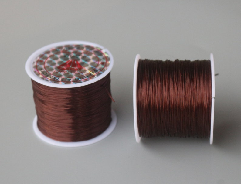May include: Two spools of brown elastic cord, wound on white plastic spools. The spools have a holographic label with the text "Elastic Cord & String".
