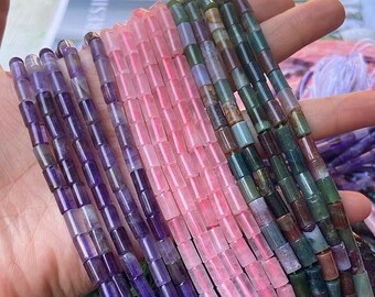 May include: A strand of purple, pink, and green gemstone beads. The beads are all cylindrical and have a smooth, polished finish. The beads are strung on a clear elastic cord.