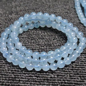 Könnte beinhalten: Ein hellblaues Aquamarin-Armband mit runden Perlen. Das Armband besteht aus mehreren Perlensträngen und wird auf einer dunkelgrauen, strukturierten Oberfläche gezeigt.