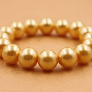Könnte beinhalten: Ein goldfarbenes Perlenarmband mit schlichtem Design. Das Armband besteht aus runden Perlen, die auf einer durchsichtigen Gummikordel aufgereiht sind.