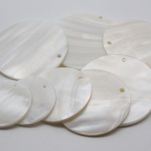 May include: A collection of white mother of pearl round discs with holes for hanging. The discs are various sizes and have a pearlescent sheen.