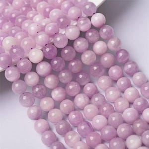 May include: A strand of pale lavender round gemstone beads. The beads are smooth and polished, with a subtle shimmer.