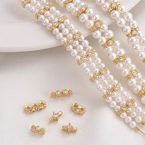 Puede incluir: Tres hileras de collares de perlas blancas con detalles dorados y pequeños diamantes de imitación transparentes. Los collares están dispuestos sobre una superficie blanca con varios pequeños conectores dorados con diamantes de imitación transparentes.