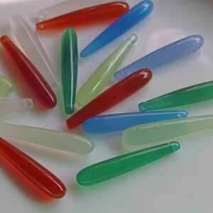 Puede incluir: Un conjunto de cuentas alargadas en forma de lágrima, en varios colores: rojo, verde, azul y blanco. Estas cuentas translúcidas tienen un acabado liso y pulido y un pequeño agujero en un extremo, para la creación de joyas.