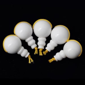 Könnte beinhalten: Fünf weiße Keramik-Gebetsperlen mit gelben Quasten. Die Perlen sind rund und haben eine leicht strukturierte Oberfläche.