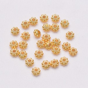 May include: A collection of 20 gold-coloured metal beads with a round, flat, and slightly raised centre. Each bead has a decorative design of small circles around the centre.
