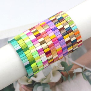 May include: A stack of colourful square tile bracelets in various shades of green, pink, yellow, blue, and orange. The bracelets are made of ceramic tiles with a glossy finish.