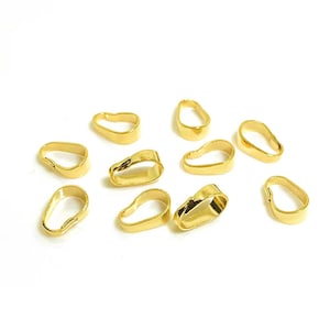 May include: Ten gold-coloured metal pendant bails, each with a slightly different shape, are scattered on a white surface.