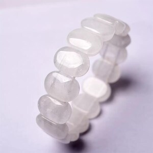 Op de afbeelding: Een witte edelsteenarmband. De armband bestaat uit ovaalvormige, gepolijste stenen die aan elkaar zijn geregen. De stenen hebben een doorschijnende kwaliteit en het algehele uiterlijk is glad en elegant. De armband staat tegen een witte achtergrond.