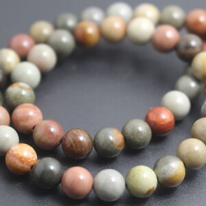 Könnte beinhalten: Eine Kette aus mehrfarbigen Edelsteinperlen. Die Perlen sind rund und haben verschiedene Farben, darunter Braun, Beige, Rot und Grün. Die Perlen sind auf einer durchsichtigen Schnur aufgefädelt.