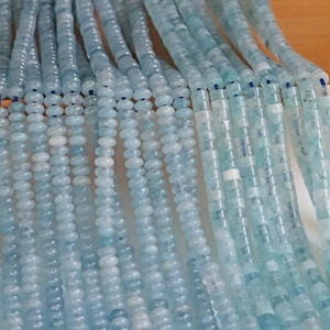 Puede incluir: Primer plano de varios hilos de cuentas de aguamarina azul claro. Las cuentas son redondas y tienen un acabado liso y pulido.