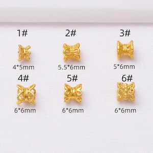 Puede incluir: Seis cuentas decorativas doradas con diseños únicos. Las medidas varían de 4 mm x 5 mm a 6 mm x 6 mm. Se muestran sobre una superficie blanca.