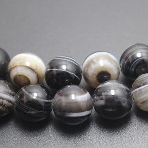 May include: A strand of black and white agate beads. The beads are round and have a polished finish. The beads are strung on a clear elastic cord.