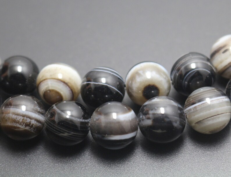May include: A strand of black and white agate beads. The beads are round and have a polished finish. The beads are strung on a clear elastic cord.