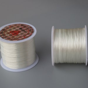 May include: Two spools of white elastic string. The spools are made of white plastic and have a red and white label that says "Strong & Elastic".