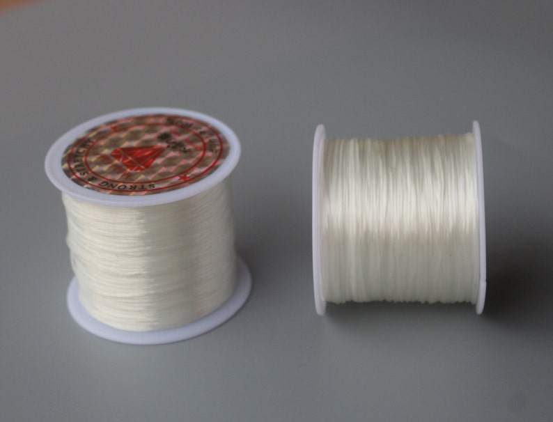 May include: Two spools of white elastic string. The spools are made of white plastic and have a red and white label that says "Strong & Elastic".