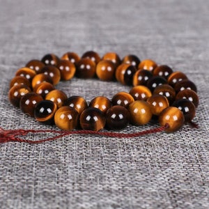 May include: A strand of round, brown and gold tiger's eye beads. The beads are strung on a thin, red cord.