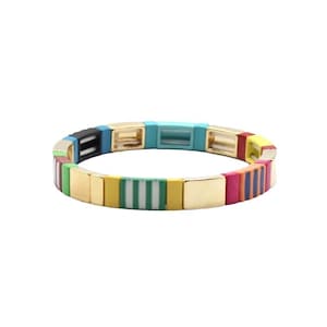 Könnte beinhalten: Ein farbenfrohes Stretch-Armband mit goldenen Akzenten. Das Armband besteht aus kleinen, quadratischen Perlen in verschiedenen Farben, darunter Rot, Orange, Gelb, Grün, Blau und Lila. Die Perlen sind in einem gestreiften Muster angeordnet.