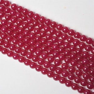 Peut inclure: Gros plan sur plusieurs brins de perles rondes rouge foncé. Les perles sont lisses et de taille uniforme, enfilées sur un fin cordon rouge. Les perles ont une finition brillante. Idéal pour la création de bijoux.