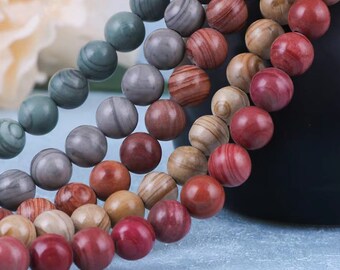 May include: A strand of colorful gemstone beads in shades of red, brown, gray, and green. The beads are round and have a natural, polished finish.