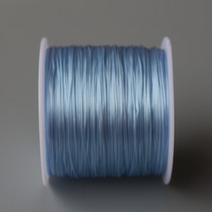 Peut inclure: Une bobine de cordon &eacute;lastique bleu clair, enroul&eacute;e autour d'une bobine en plastique blanc.
