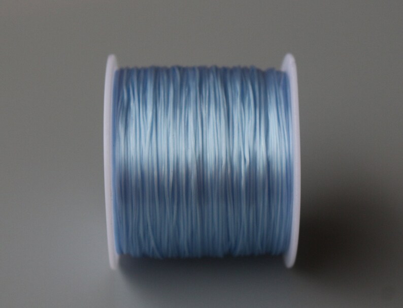Peut inclure: Une bobine de cordon &eacute;lastique bleu clair, enroul&eacute;e autour d'une bobine en plastique blanc.