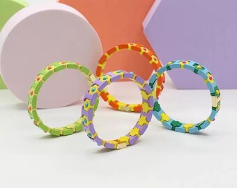 Puede incluir: Cuatro pulseras coloridas con un diseño de flores. Las pulseras están hechas de azulejos de cerámica y tienen un cierre dorado. Las pulseras están dispuestas en círculo sobre una superficie blanca.