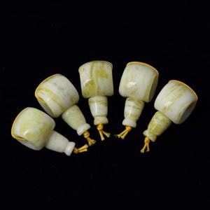 Peut inclure: Cinq bouchons de bouteille de couleur jade avec un design cylindrique et une ficelle dorée. Les bouchons ont un aspect marbré avec des teintes blanches et vertes. Le fond est noir.