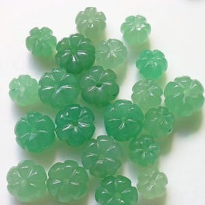 Op de afbeelding: Een verzameling groene jade bloemen kralen. De kralen zijn glad en gepolijst, met een delicaat bloemenpatroon.