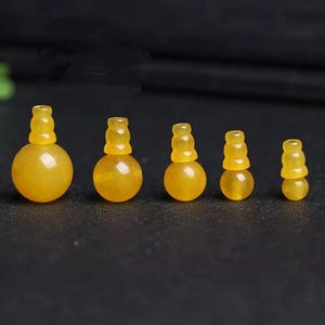 Peut inclure: Cinq pendentifs en pierres précieuses jaunes, chacun avec une base arrondie et un sommet cylindrique empilé. Les pendentifs varient en taille, le plus grand à gauche et le plus petit à droite. Les pierres précieuses sont translucides.