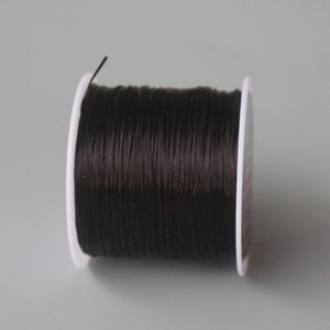 May include: A spool of black elastic cord wound around a white plastic bobbin.