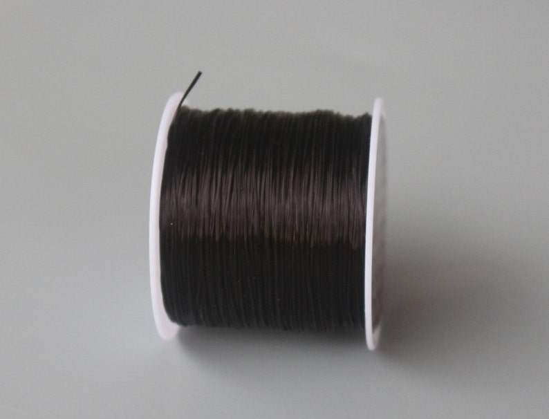 May include: A spool of black elastic cord wound around a white plastic bobbin.