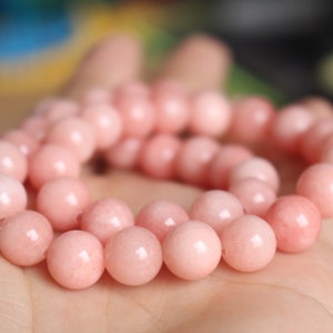 Puede incluir: Una hebra de cuentas de piedras preciosas rosadas, probablemente cuarzo rosa, enhebradas en un hilo transparente. Las cuentas son lisas y redondas, con un brillo sutil.