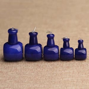 May include: Five bottle-shaped objects in a deep blue hue are displayed. Each has a rounded base, a slender neck, and a small loop at the top. The objects are of different sizes and appear to be made of a polished material.