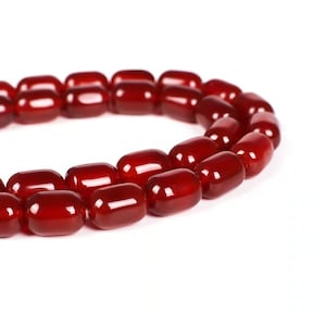 May include: A strand of red carnelian beads, each bead is oval shaped and polished to a smooth finish.